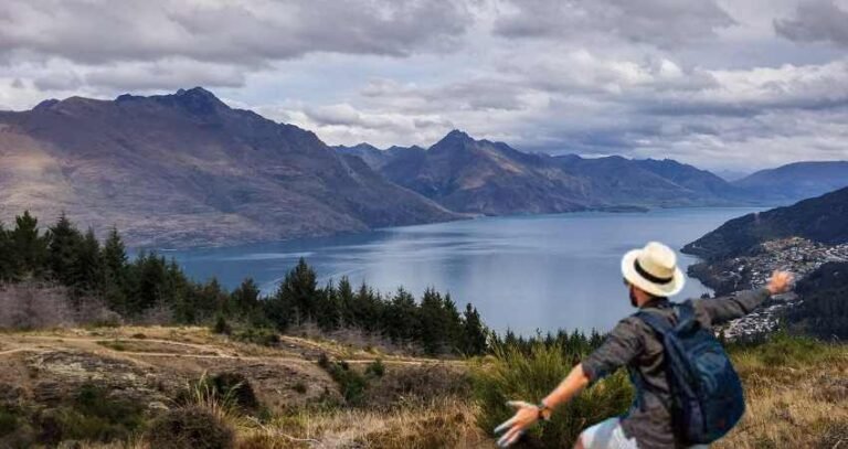 Traveler with backpack enjoying a panoramic mountain and lake view under cloudy skies.
