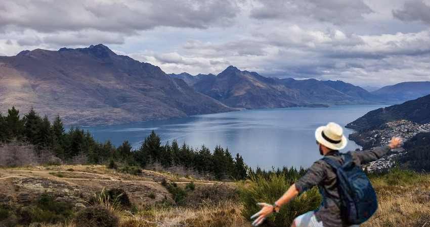 Traveler with backpack enjoying a panoramic mountain and lake view under cloudy skies.